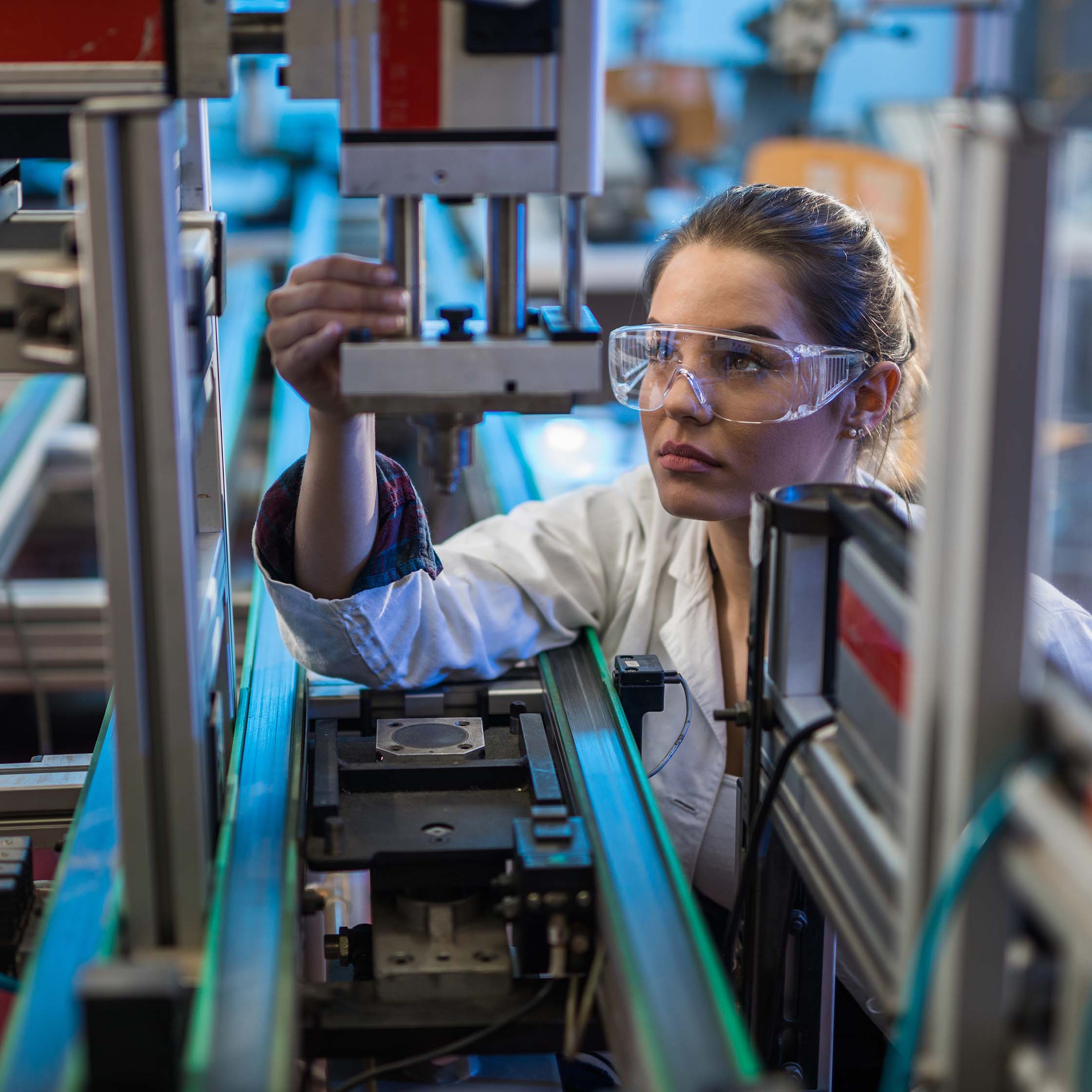 Female Worker wearing safety glasses inspecting a assembly line robot arm