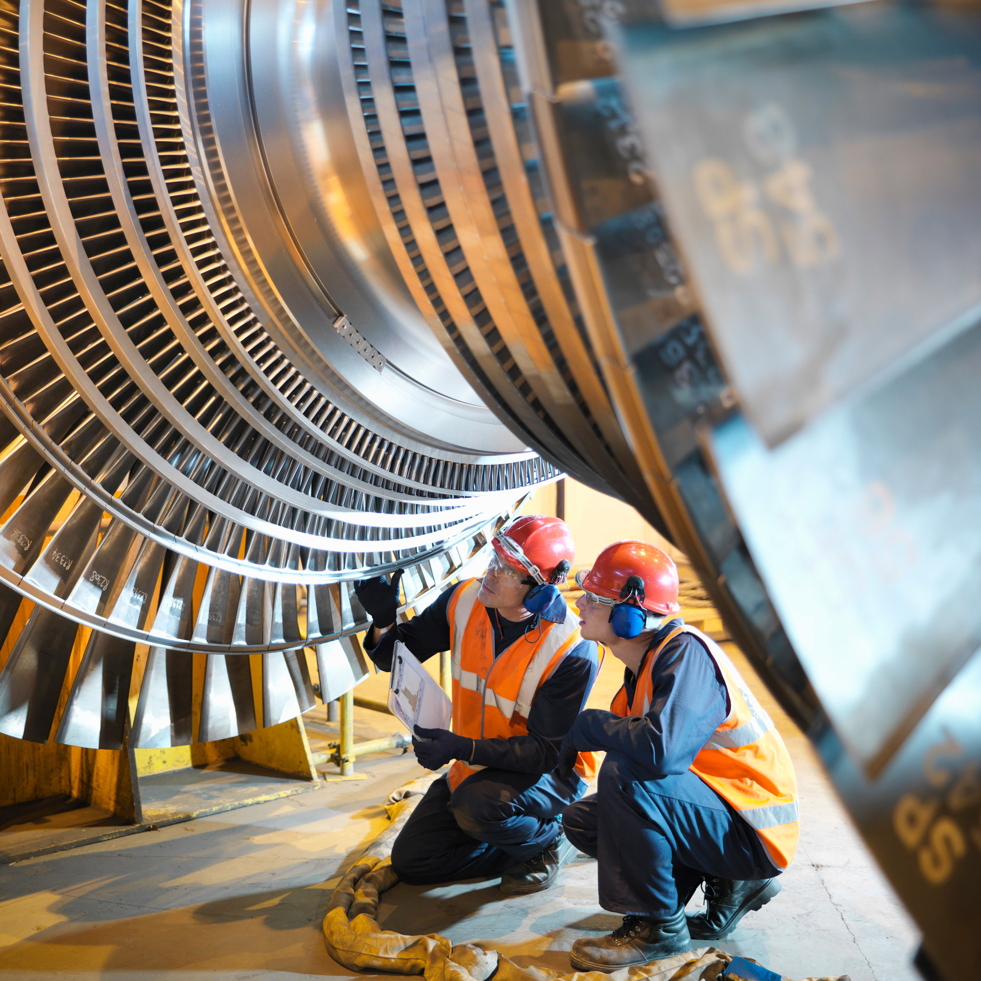 Two workers wearing safety gear inspecting a cargo ship engine component