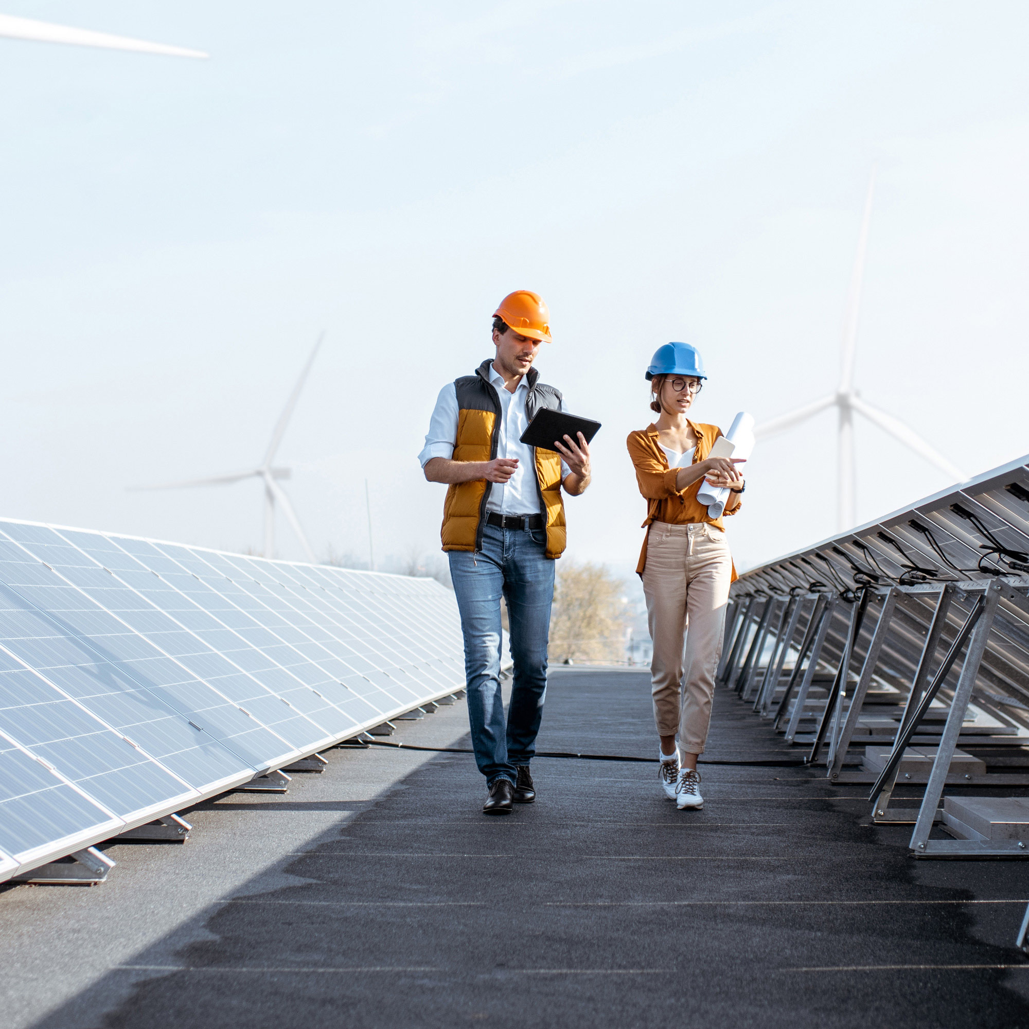 A man and a woman wearing hard hats walking between two rows of solar panels